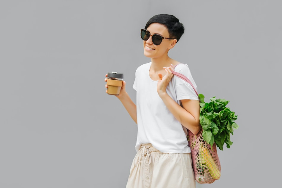 Young woman in light summer clothes with a eco bag of vegetables, greens and reusable coffee mug. Sustainable lifestyle. Eco friendly concept.