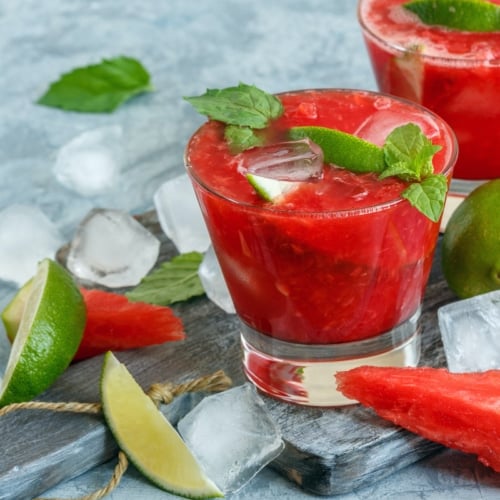 Glasses of watermelon mojito, slices of lime, mint and ice on the serving board.