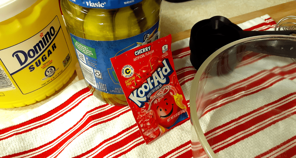 Mixing cherry Kool-Aid powder into pickle brine in a jar