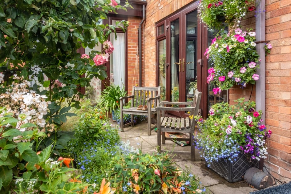 A pair of wooden chairs in a corner of a garden.