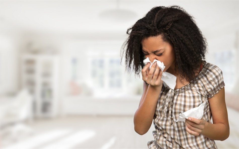 Young woman sneezing into a tissue.