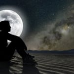 Profile of a woman sitting on sand in the moonlight.