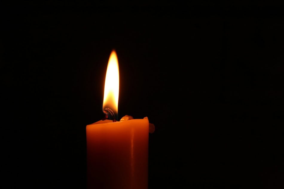 Single lit candle flame in darkness for spiritual self-care practice.