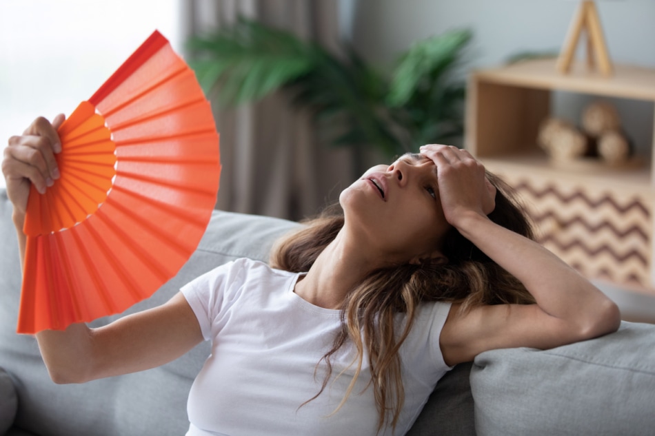 overheated woman fanning herself with an orange fan.