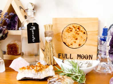 Full moon ritual items including Moon Water, a candle, herbs, and crystals.