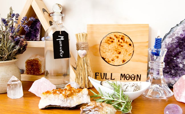 Full moon ritual items including Moon Water, a candle, herbs, and crystals.