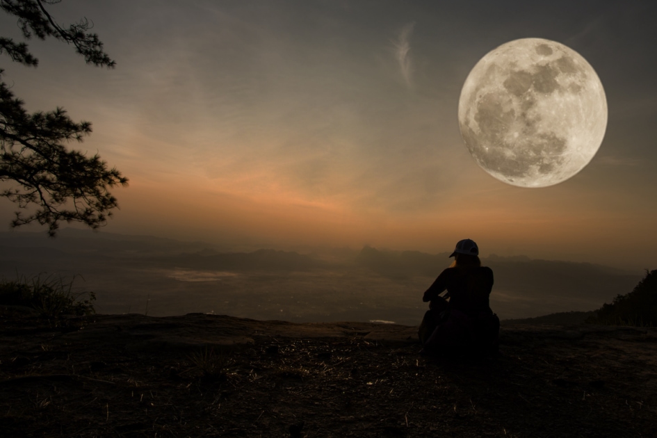woman sitting serenely of the cliff and looking at the valley and mountains with moon