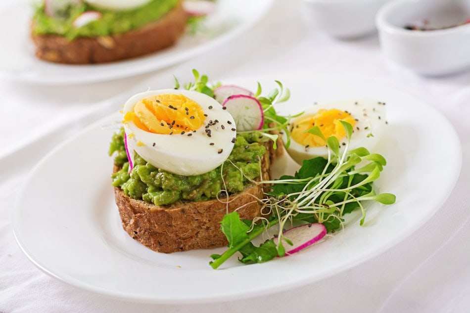 Healthy food. Breakfast. Avocado egg sandwich with whole grain bread on white wooden background.