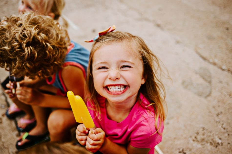 Young smiling girl eating an ice pop.