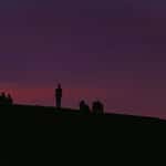 People watching the full moon from a hill at dusk.