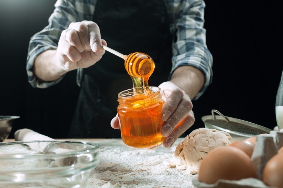 Professional male cook pours honey into a jar.