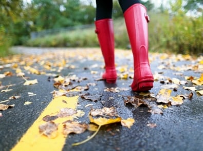 Autumn fall concept with colorful leaves and rain boots outside. Close up of woman feet walking in red boots.