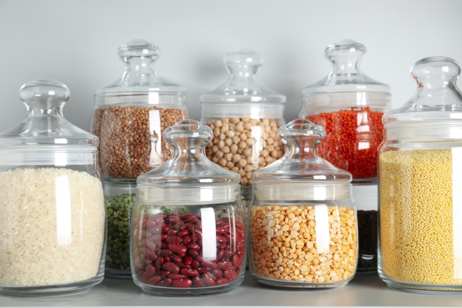 Glass jars with different types of groats and pasta on white shelf