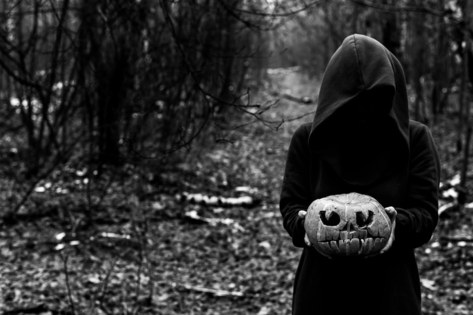 A witch holds a creepy pumpkin in a dense autumn forest. Jack o lantern for halloween. Monochrome.