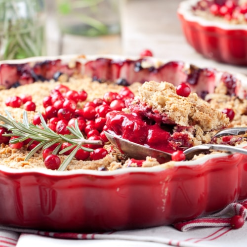 Cranberry apple crumble with rosemary on a wooden and textile background.