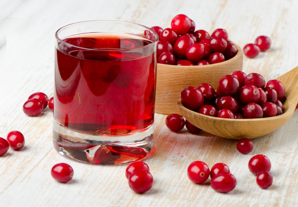 Cranberries in a  wooden spoon and glass of juice. Selective focus