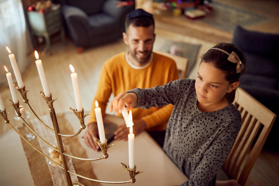 Little girl and her father light menorah candles on Hanukkah at home.