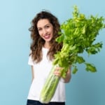 Young woman holding a celery isolated on blue background with happy expression.