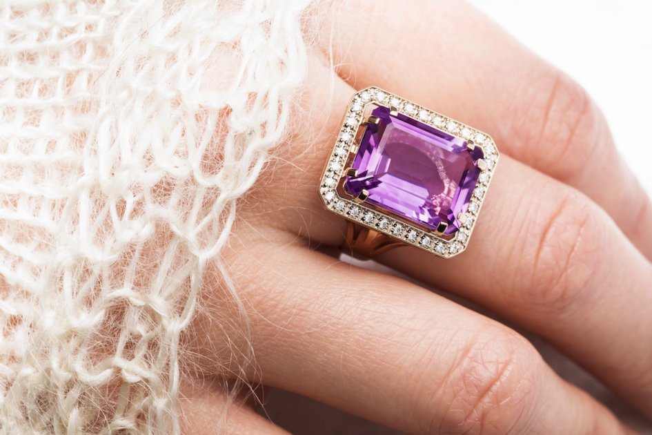 Beautiful golden ring with a large amethyst on a female hand, close-up.