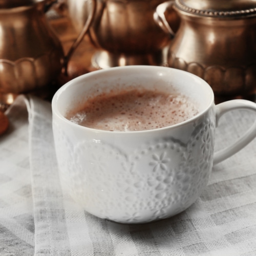 Cup of hot cacao on cotton serviette against silver service.