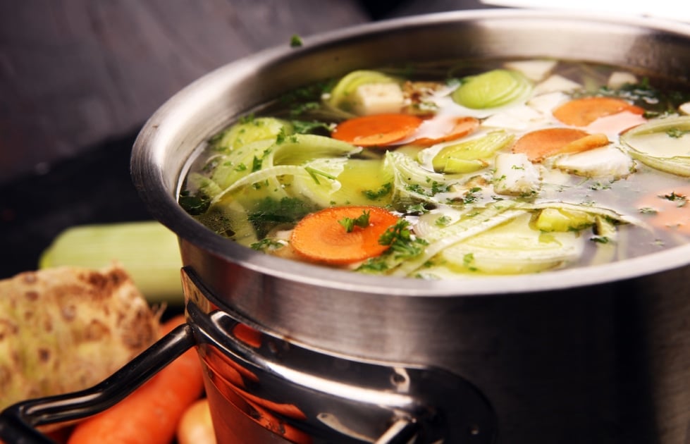 Broth with carrots, onions various fresh vegetables in a pot - colorful fresh clear spring soup. Rural kitchen scenery vegetarian bouillon.