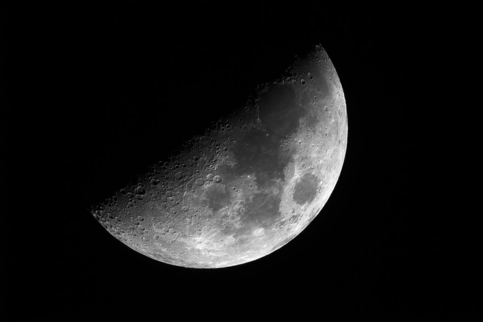 Close up of bright Moon in first quarter phase with detailed craters in the shadow, taken with telescope, isolated in dark background.