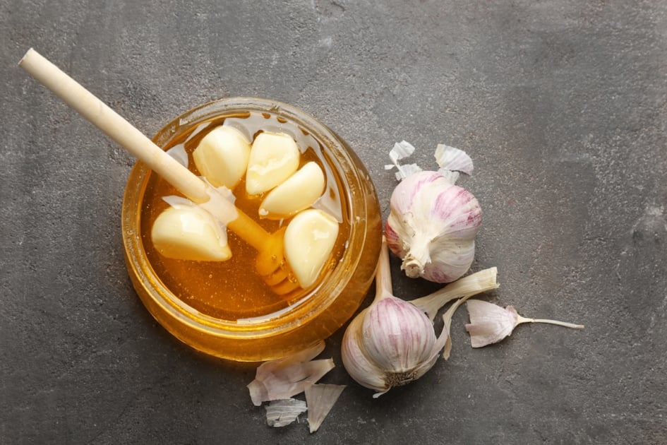 Glass jar with honey and garlic on grey textured background, top view