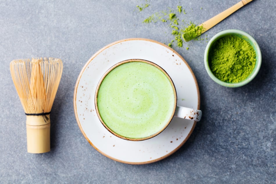 Matcha green tea latte in a cup with bamboo whisk. Top view.