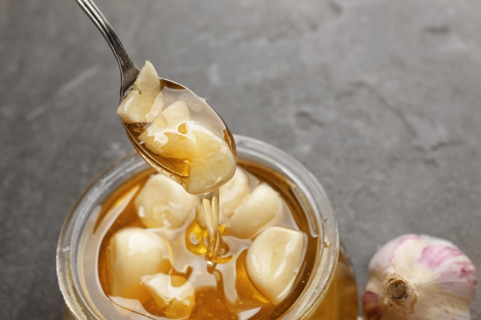 Spoon over glass jar with honey and garlic on grey textured background