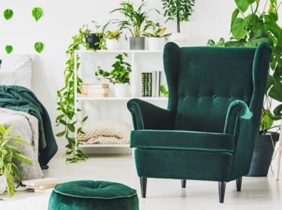 Emerald green comfortable armchair and pouf in contemporary bedroom interior with urban jungle.