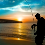 A man fishing from a beach at dusk.