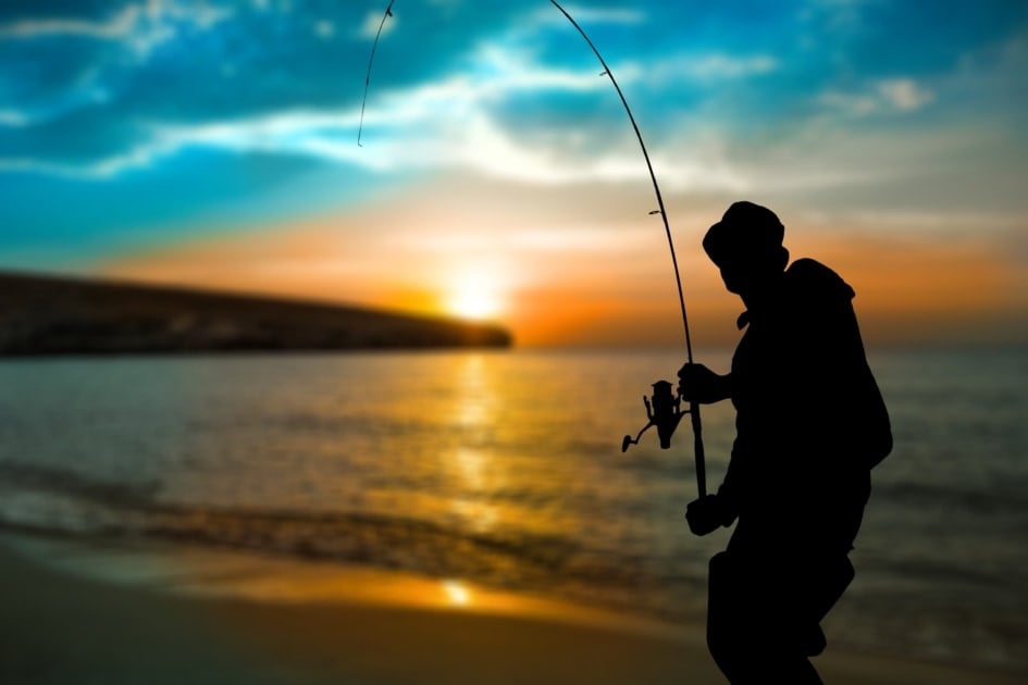 A man fishing from a beach at dusk.