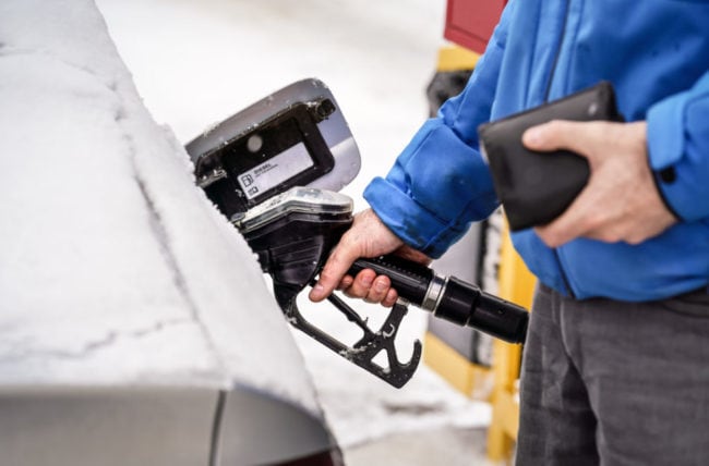 A feature image of a person putting fuel in their car wondering how to save money on gas this winter.