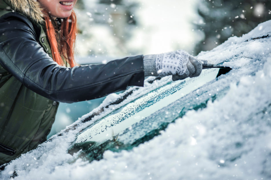 A woman scraping ice off of her windshield during Canadian winter 2021-2022.