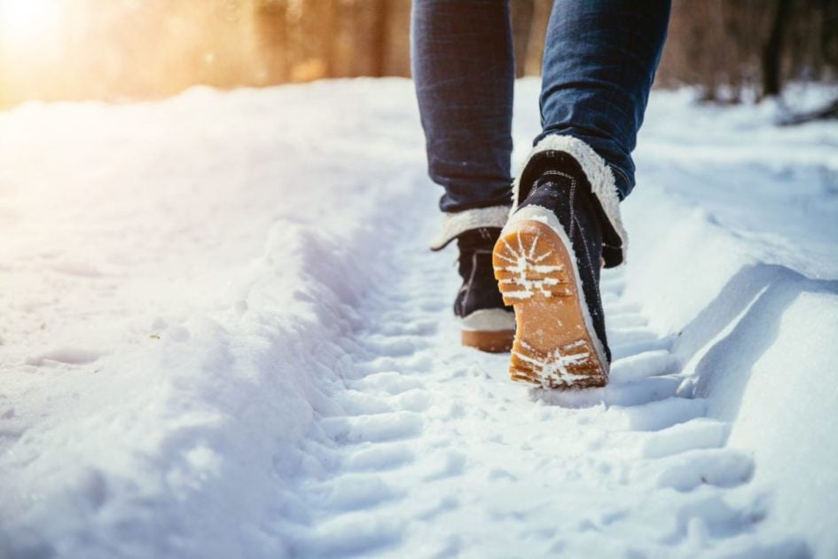 A man walking through the snow reviewing winter weather 2021-2022 forecasts.