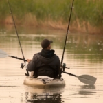 A man in a fishing kayak paddling in water.