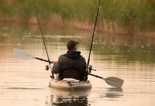 A man in a fishing kayak paddling in water.