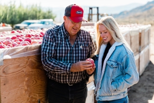Experienced apple farmer Kaitlyn Thornton with her father looking at a cosmic crisp apple.
