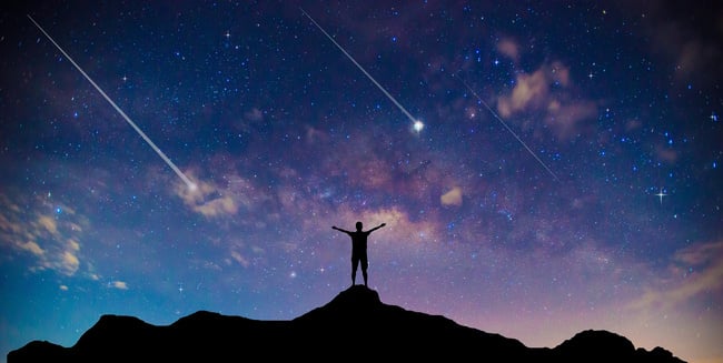 A man on a mountain celebrating shooting star superstitions and good luck.