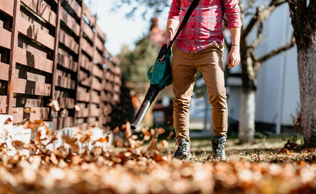 A man with a leaf blower before winterizing lawn mower and other tools.