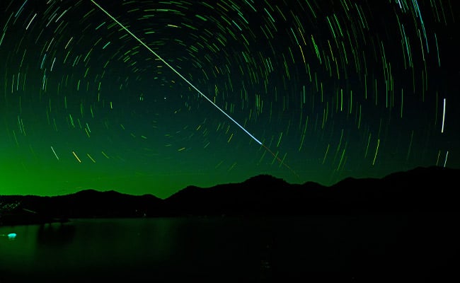 Shooting stars tonight represented by a time-lapse photo of a bright meteor streaking in the sky above a lake.