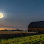 March Worm Moon astrology report represented by a full Moon beside a barn in early spring and green grass in the foreground.