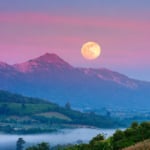 Pink Moon astrology report represented by a full Moon in a pink sky over purple and blue mountains.