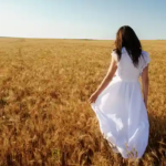 Woman wearing white after Labor Day, holding her dress as she walks through a wheat field.