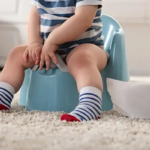 A boy toddler potty training on a blue potty.