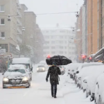 Winter weather 2024-2025 represented by a person walking down a snowy street with an umbrella.