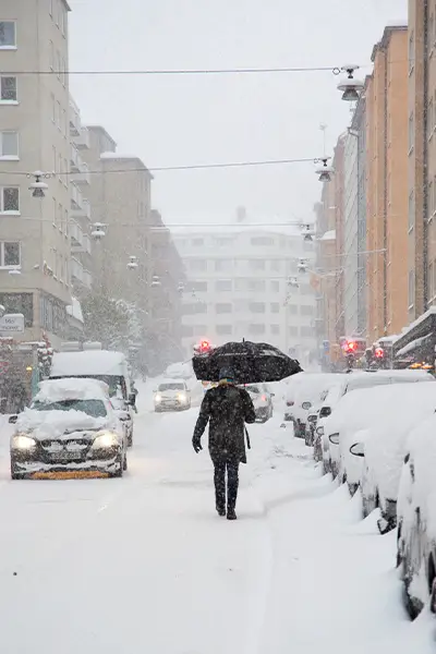 Winter weather 2024-2025 represented by a person walking down a snowy street with an umbrella.