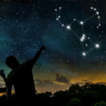 Orion stars shine brightly in the winter night sky. Silhouettes of a woman with binoculars and a man pointing them appear in the foreground.
