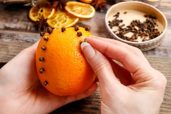 A woman placing cloves in an orange peel to create a pomander.