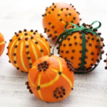 Pomanders made out of oranges and cloves. One pomander has a green ribbon tied around it.